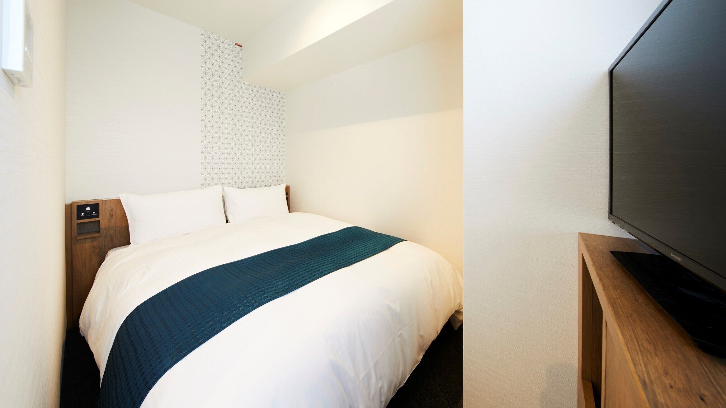 Een hotelkamer met een bed, een houten nachtkastje, een televisie en een behang met een patroon.