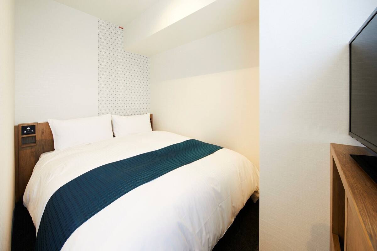 Hotellihuone, jossa on sänky, puinen yöpöytä, televisio ja kuviollinen seinä.