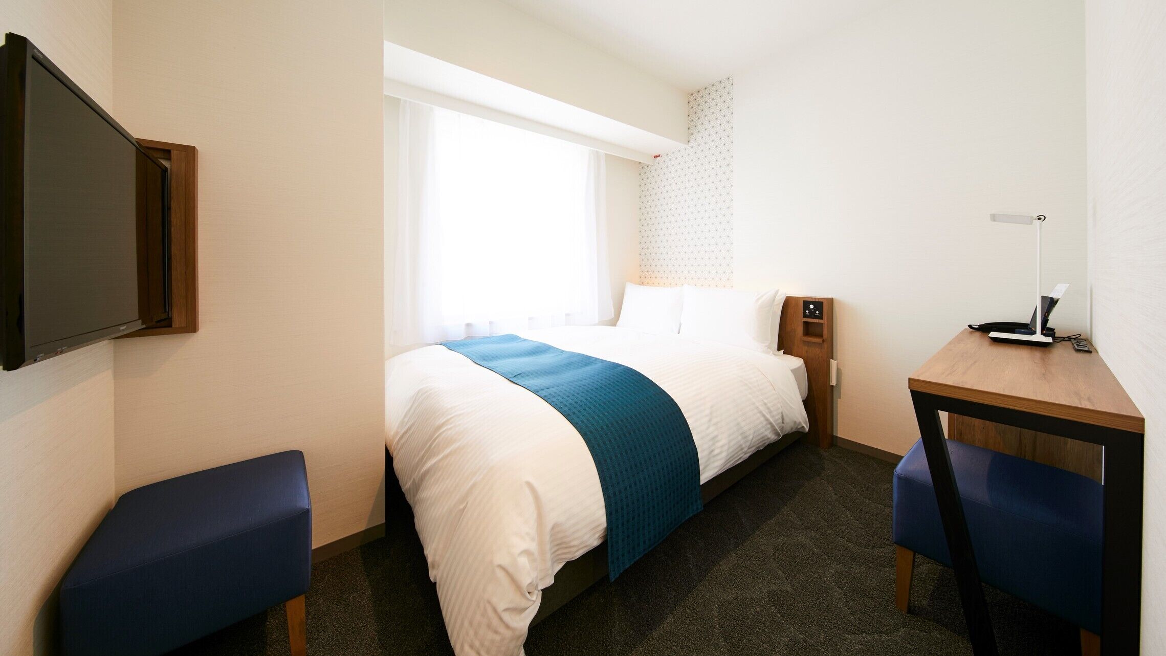 Een hotelkamer met een bed, een bureau met een laptop, een televisie en een raam met gordijnen.