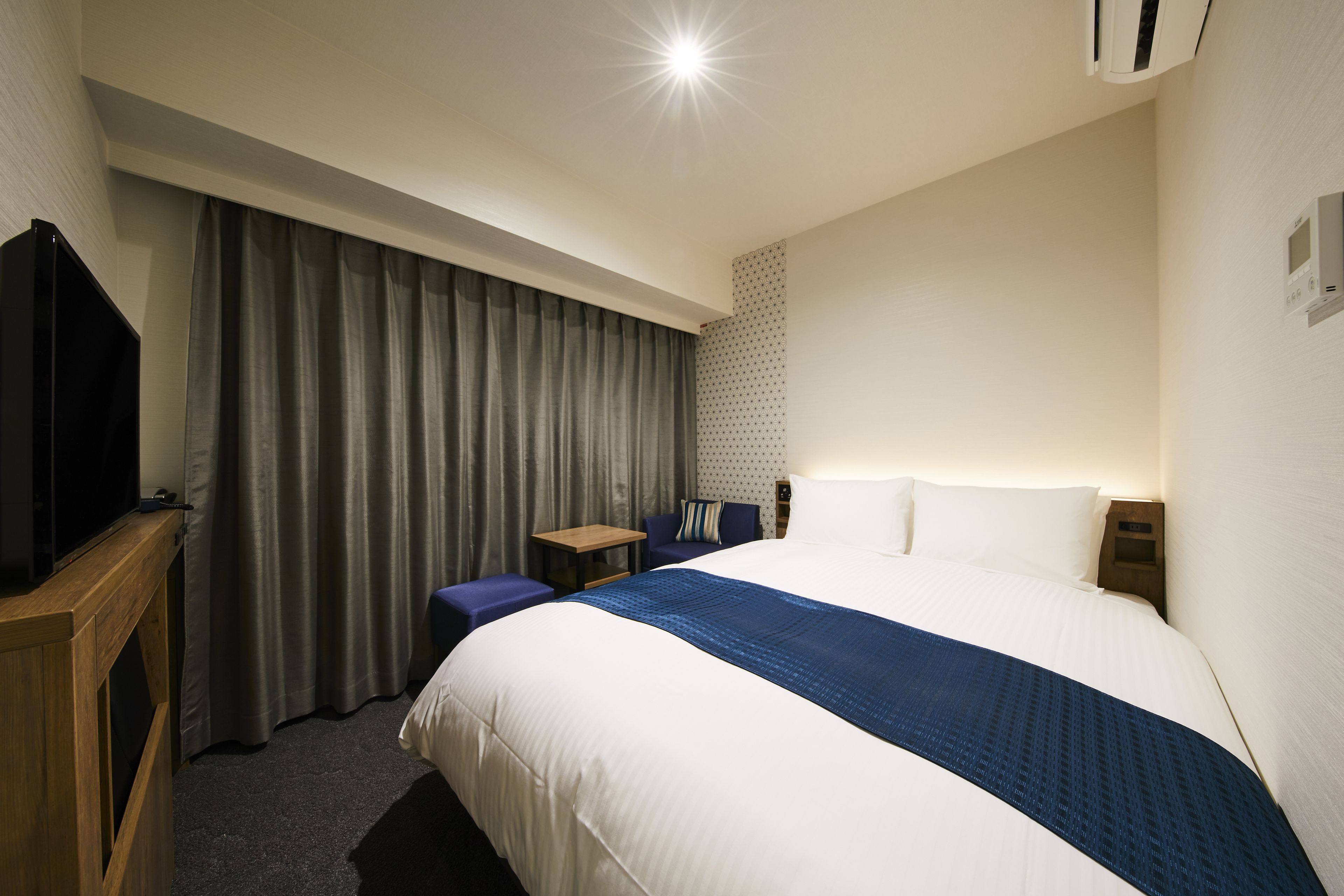 Une chambre d’hôtel avec un grand lit, un téléviseur posé sur un meuble en bois, une petite table et une chaise.