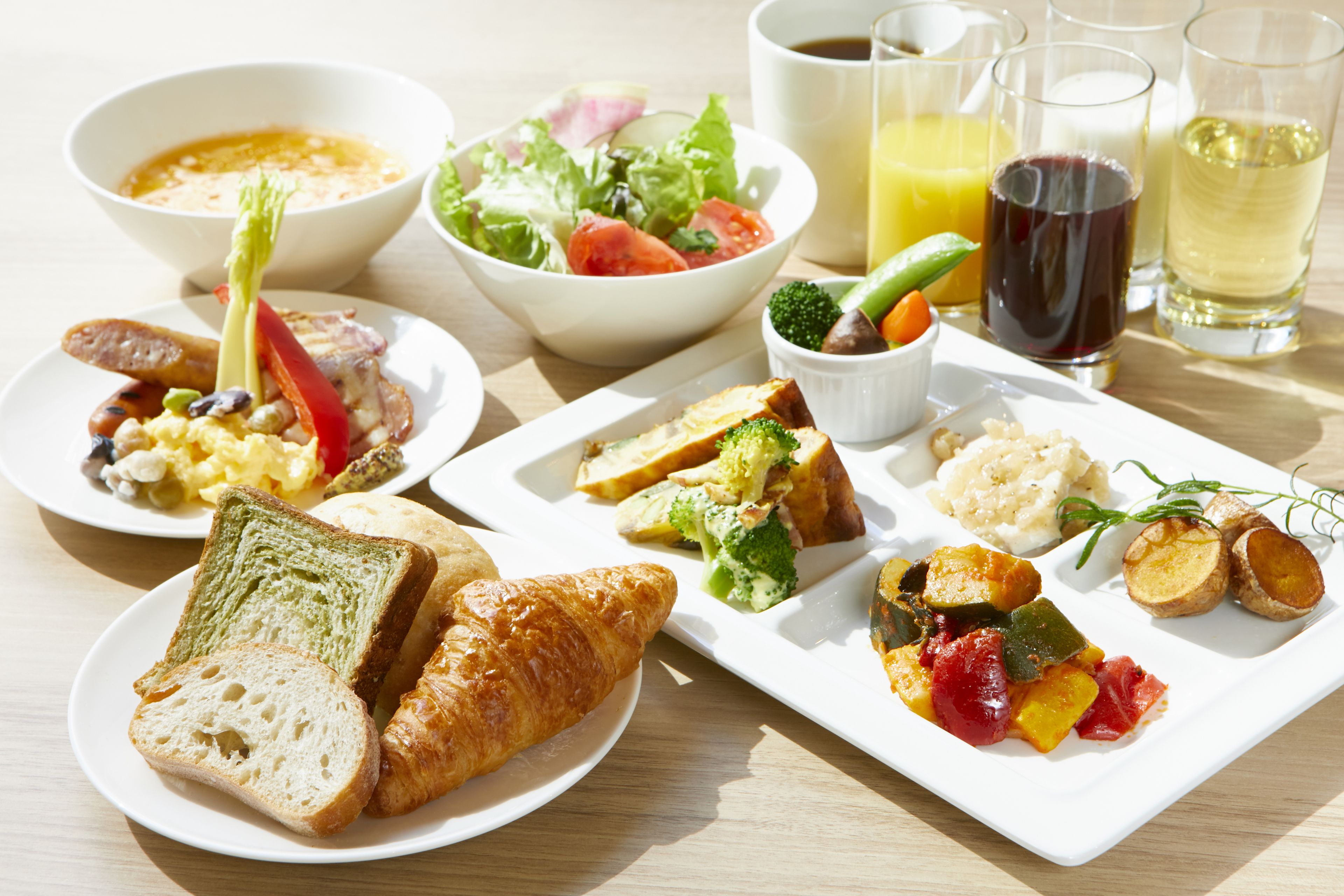 A breakfast setting with various dishes including toast, croissants, vegetables, and beverages.