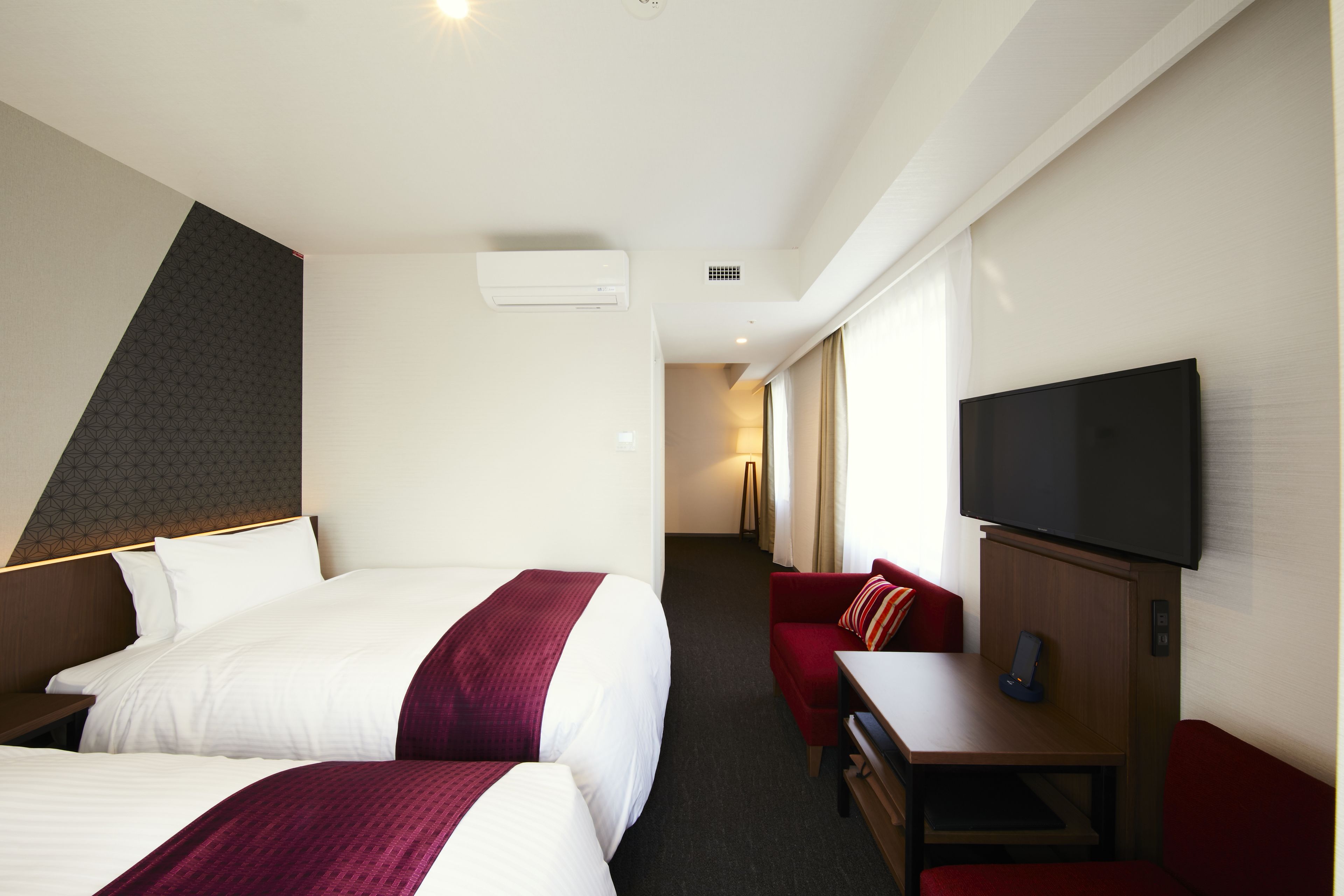 Una habitación de hotel con dos camas, televisión, escritorio y sofá rojo.