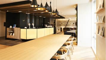 A modern restaurant with a long wooden table, black pendant lighting, and a bar area.