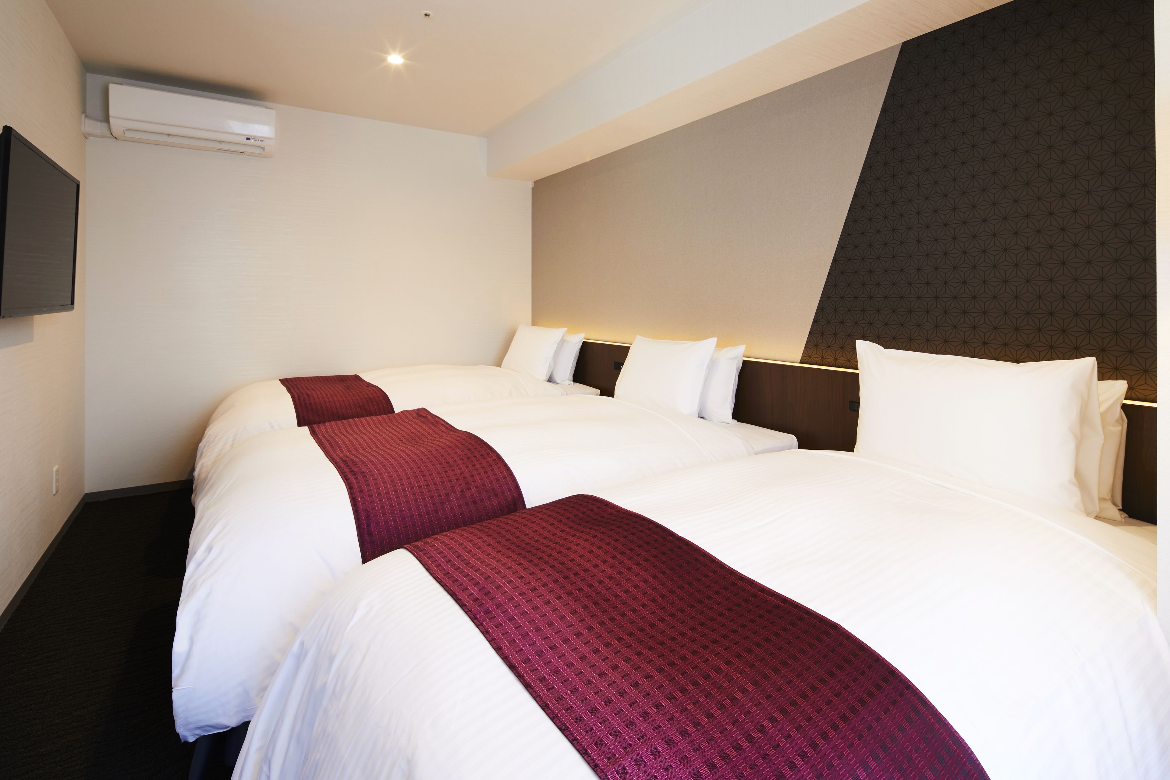 A hotel room with two beds, a flat-screen TV mounted on the wall, and a patterned wall design.