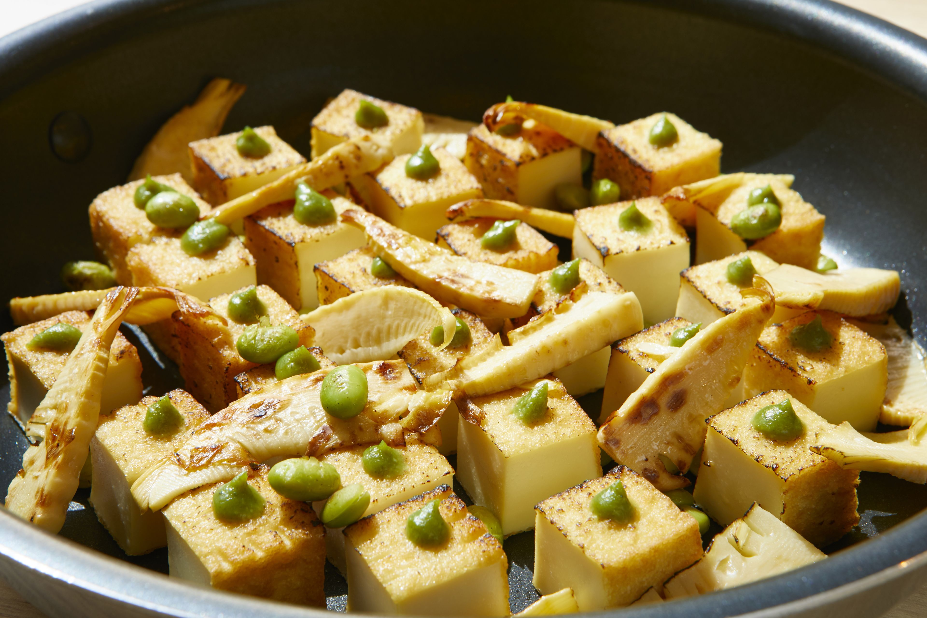 Cubos de tofu con guisantes verdes en una sartén.