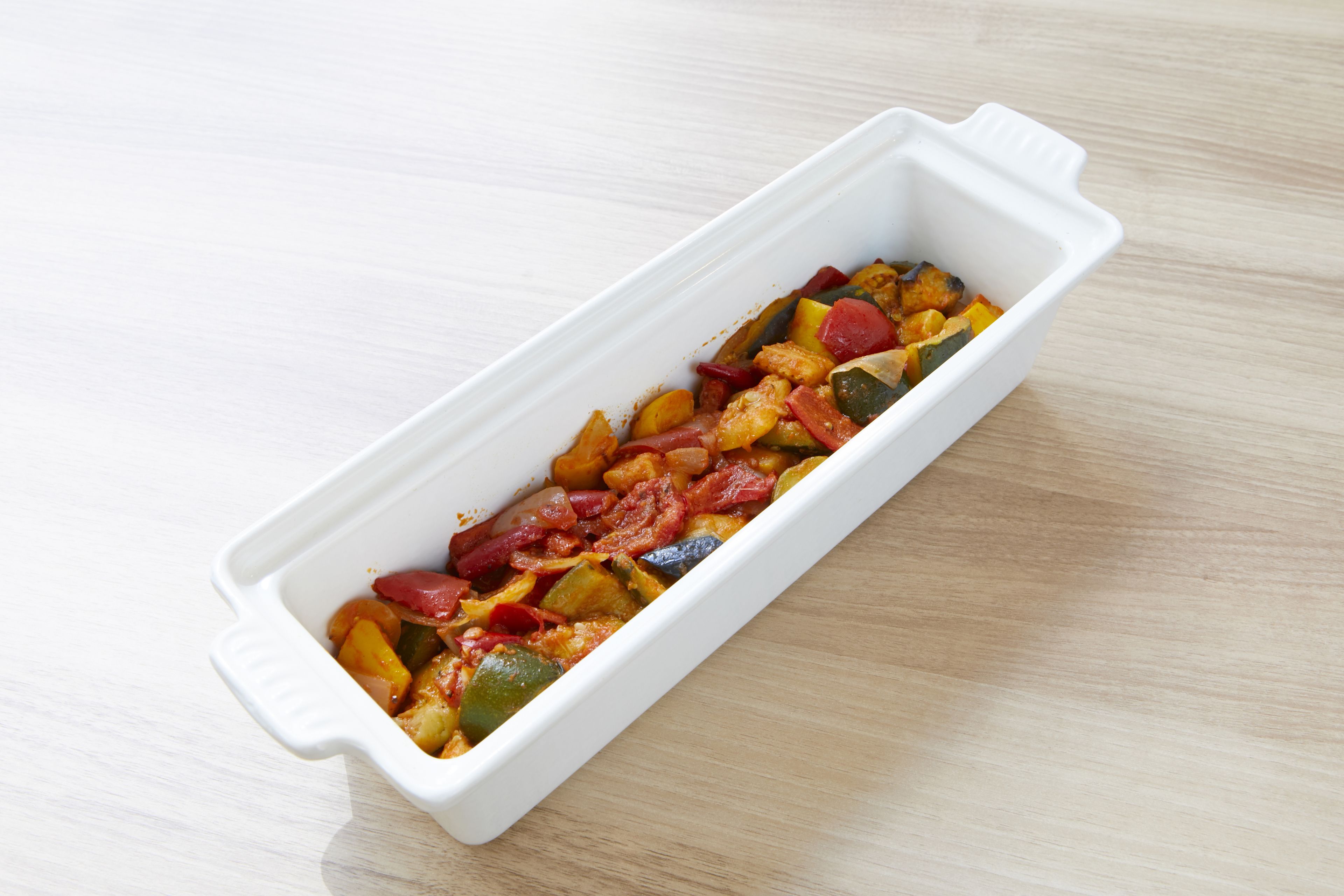 A white rectangular dish containing a variety of vegetables on a wooden surface.