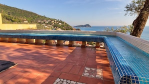 Una piscina con bordo piastrellato, circondata da piastrelle in terracotta e vista sul mare e su una collina.