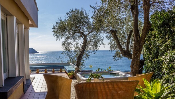Un balcone con sedie in vimini, una vasca idromassaggio e vista sul mare.