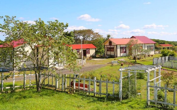 A rural setting with multiple buildings, including a main house with a red roof, surrounded by a fenced area and lush greenery.