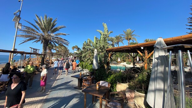 A beachside walkway with palm trees, outdoor seating, and a pool area. - ´Beach & Golf' Large Family Villa, Huge Garden, Private Pool, 350m to the Beach. (Marbella)