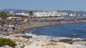 A beach with rocky foreground, people sunbathing, and buildings in the background. - ´Beach & Golf' Large Family Villa, Huge Garden, Private Pool, 350m to the Beach. (Marbella)
