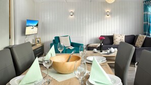 Una sala de estar moderna con una mesa de comedor de madera preparada para cuatro comensales, un sofá color turquesa y un sofá gris oscuro con cojines estampados.