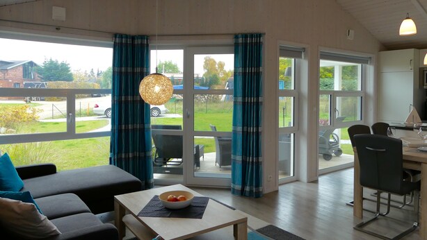 Un amplio salón con sofá, una mesa de comedor con sillas y vistas al exterior a través de grandes ventanales.