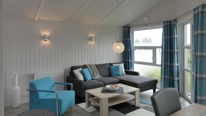 Una sala moderna con un sofá, sillones y una mesa de centro. Hay dos luces fijadas a la pared y una lámpara colgante.