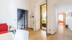 Una sala de estar moderna con un sofá rojo, una mesa blanca y una estantería. Un cuadro grande en blanco y negro adorna la pared, y un piso de madera recorre el espacio.