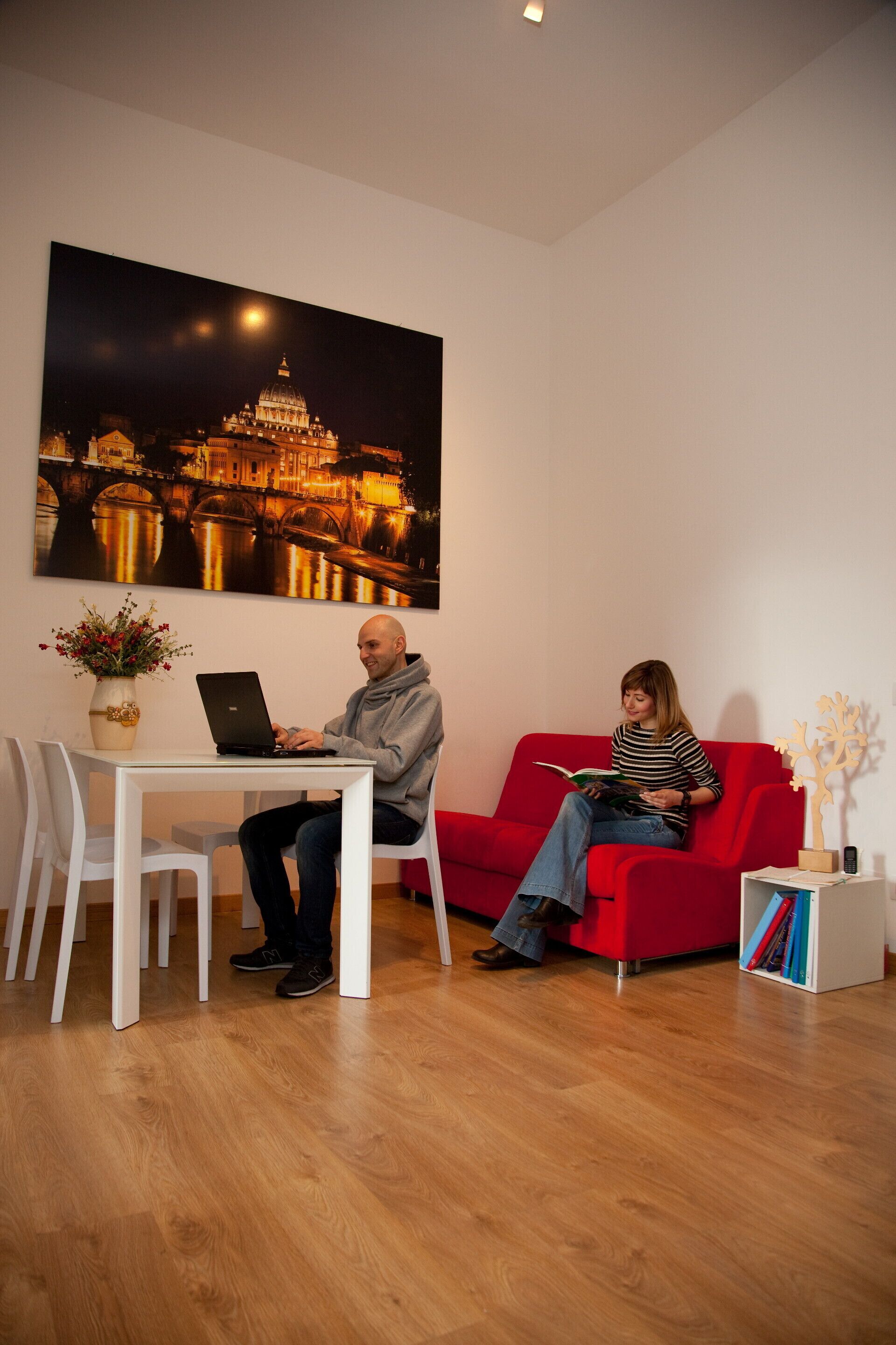 Ein Zimmer mit einem roten Sofa, einem weißen Tisch mit einem Laptop und einem großen gerahmten Bild mit einem Gebäude im Hintergrund und einem Mond.