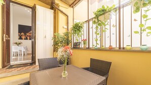 Un comedor con mobiliario de mimbre, una mesa con un jarrón de flores y vistas a la ciudad a través de un ventanal.