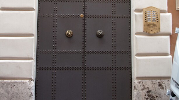 Unas puertas dobles con un escudo metálico decorativo, integradas en un arco de piedra blanca.