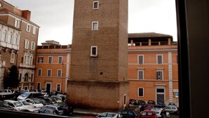 Una alta torre de ladrillo con base cuadrada y cima estrecha, rodeada de edificios históricos con numerosas ventanas y balcones.