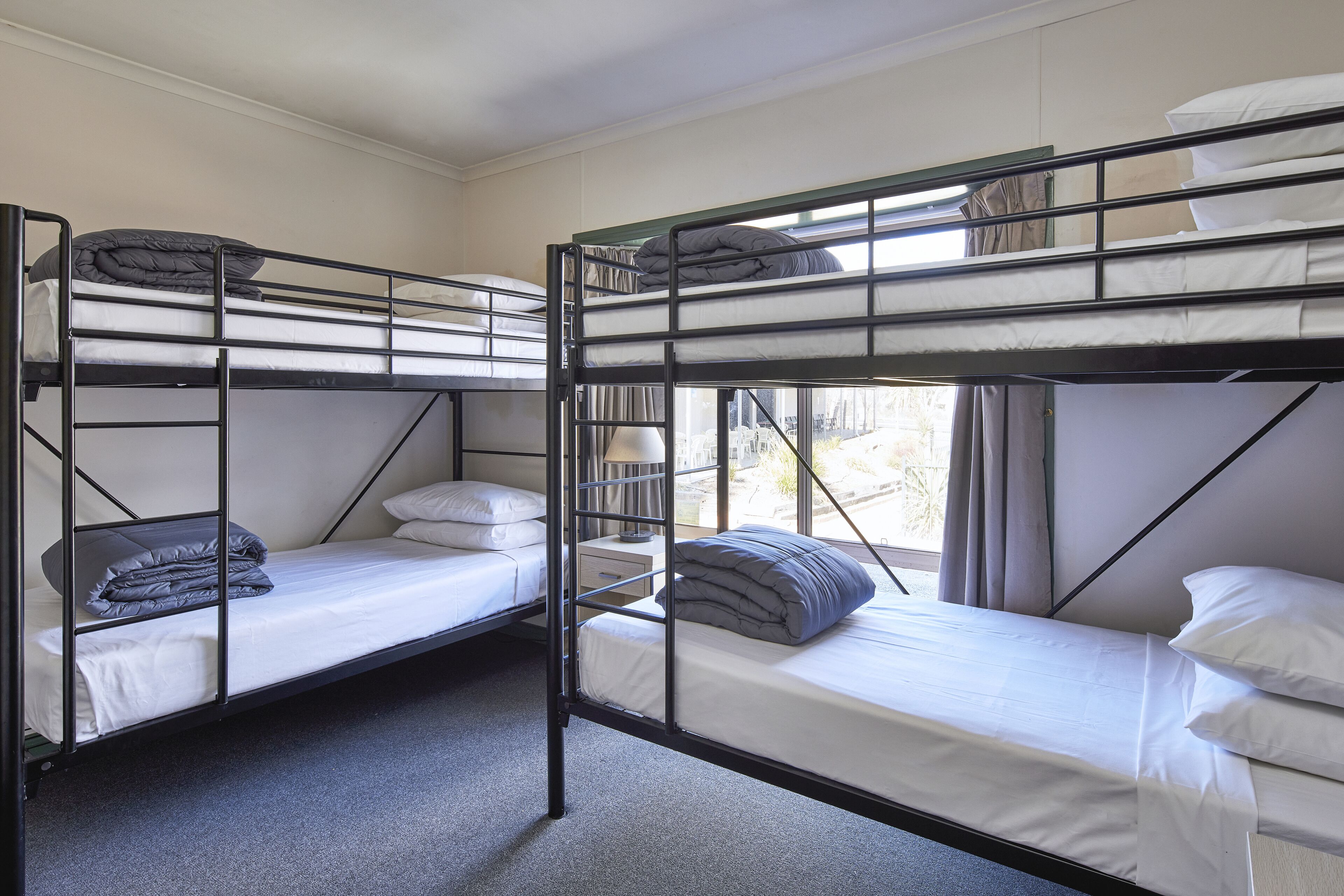 A room with bunk beds, each with a mattress and pillows, and a window providing natural light.