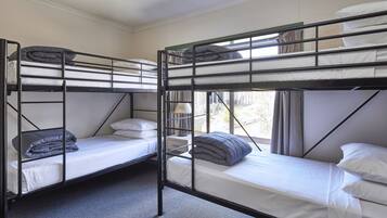 A room with bunk beds, each with a mattress and pillows, and a window providing natural light.