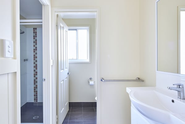 Un baño con un lavamanos blanco, un espejo y una zona de ducha con pared de azulejos.
