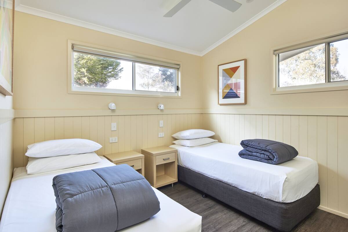 A bedroom with two beds, a nightstand, and a window.