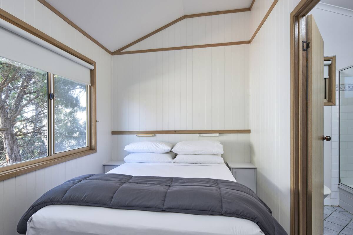 A bedroom with a bed, a window, a door, and a view of the outdoors.