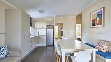 Une cuisine moderne avec des meubles blancs, un réfrigérateur encastré et un coin repas comprenant une table en bois et des chaises blanches.