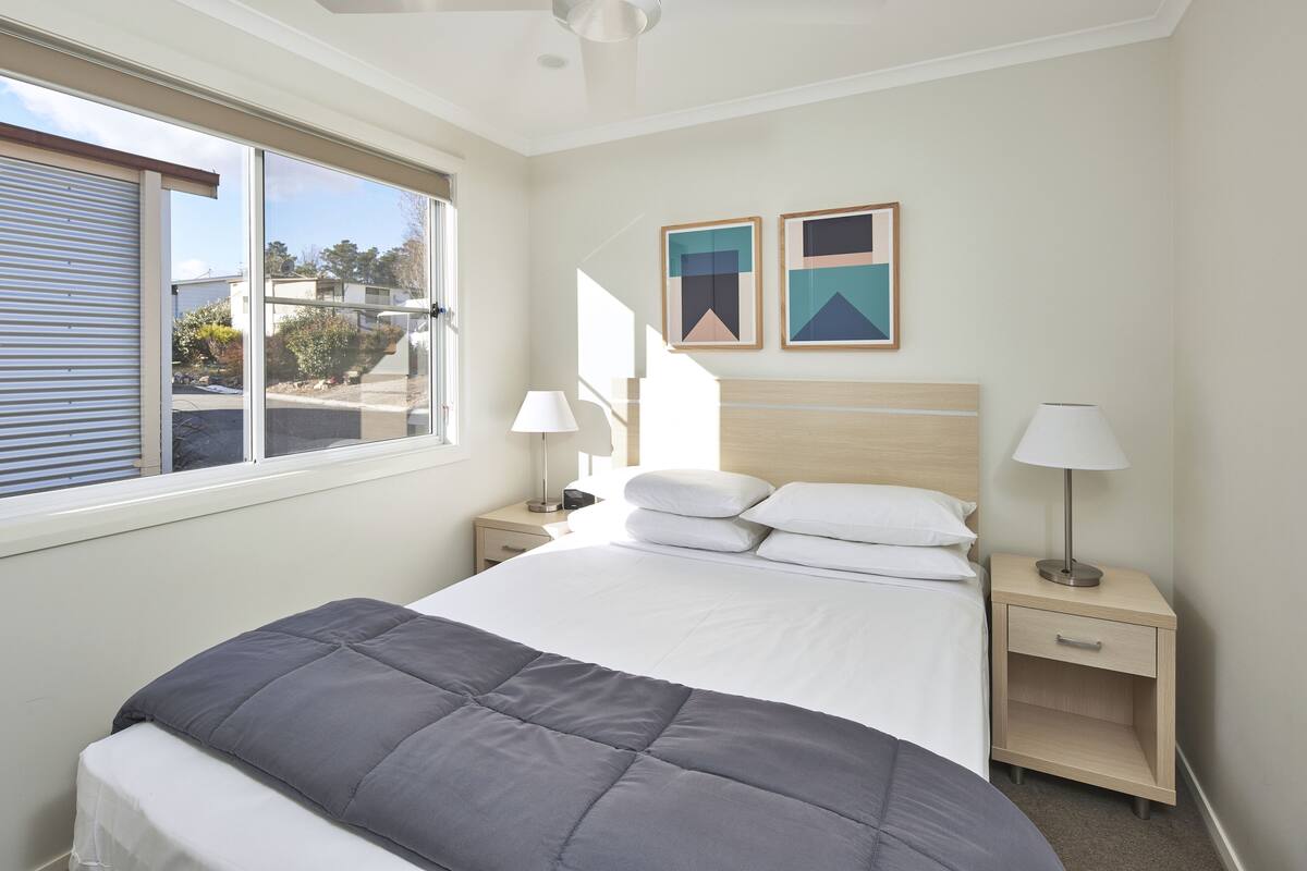 A neatly arranged bedroom with a bed, bedside tables, lamps, and two framed pictures on the wall.
