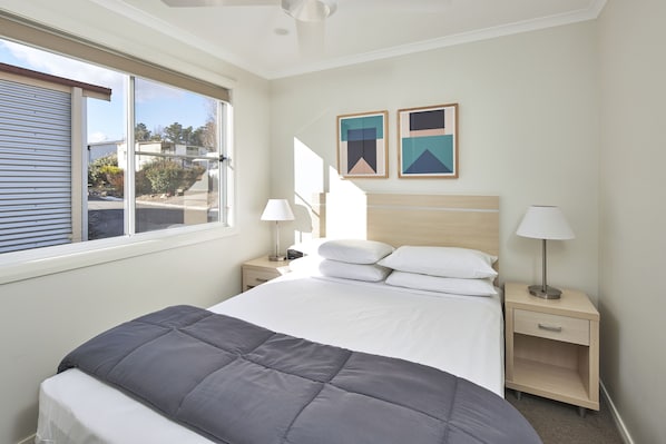 A neatly arranged bedroom with a bed, bedside tables, lamps, and two framed pictures on the wall. - NRMA Bathurst Panorama Holiday Park (Kelso)