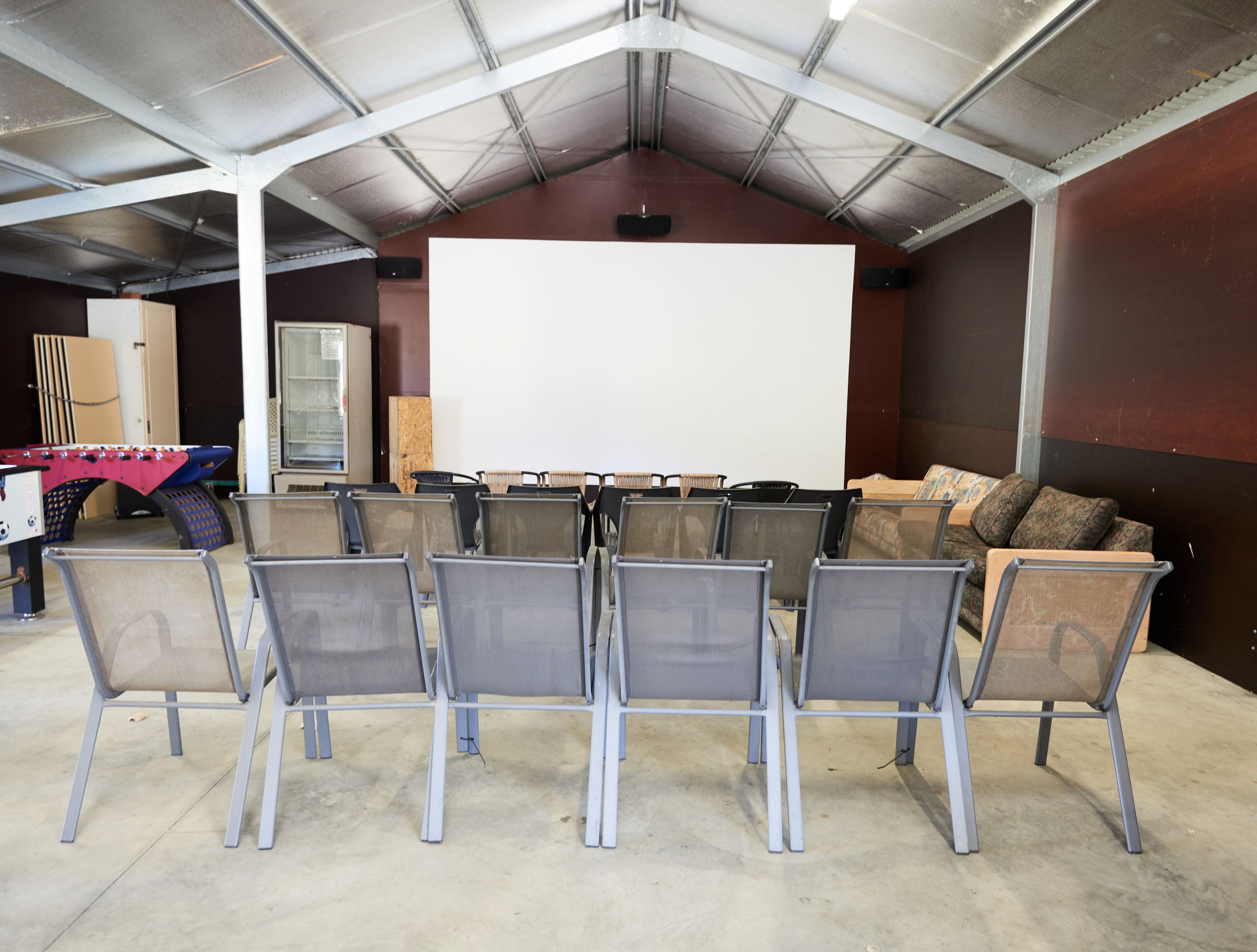 A conference room with a large white screen, rows of chairs, a sofa, and a table with a red tablecloth.