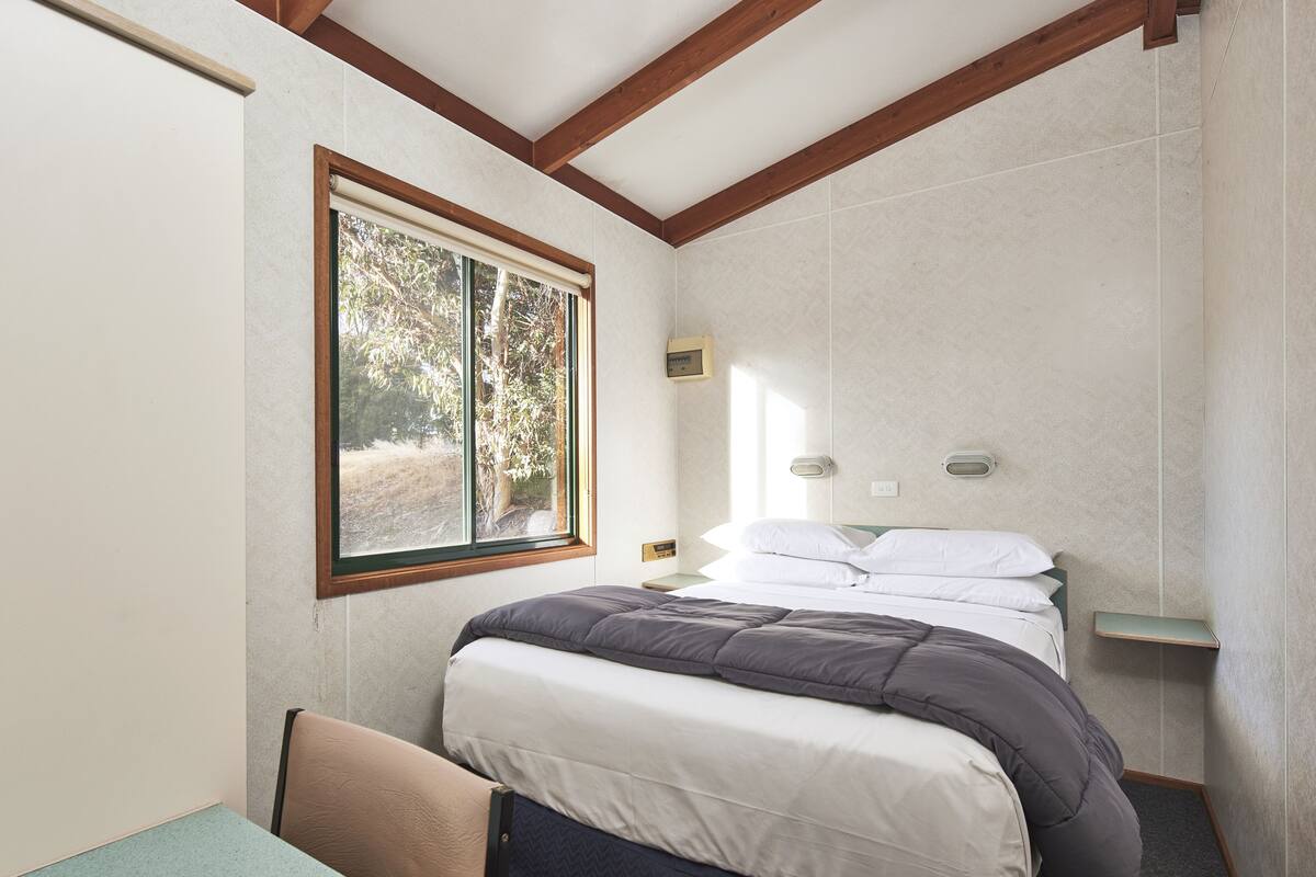 A bedroom with a bed, a window, a bedside table, and a nightstand.