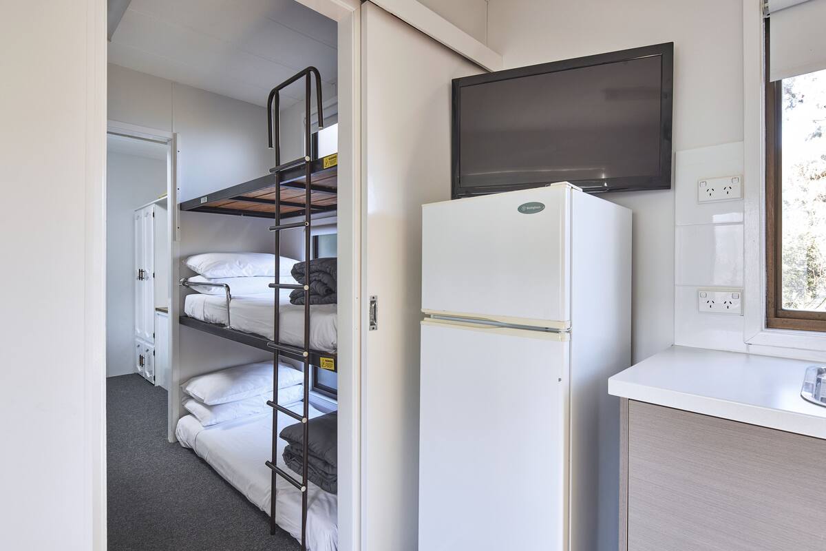 A compact room with bunk beds, a white refrigerator, a flat-screen TV, and a window with a view.