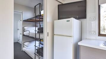 A compact room with bunk beds, a white refrigerator, a flat-screen TV, and a window with a view.
