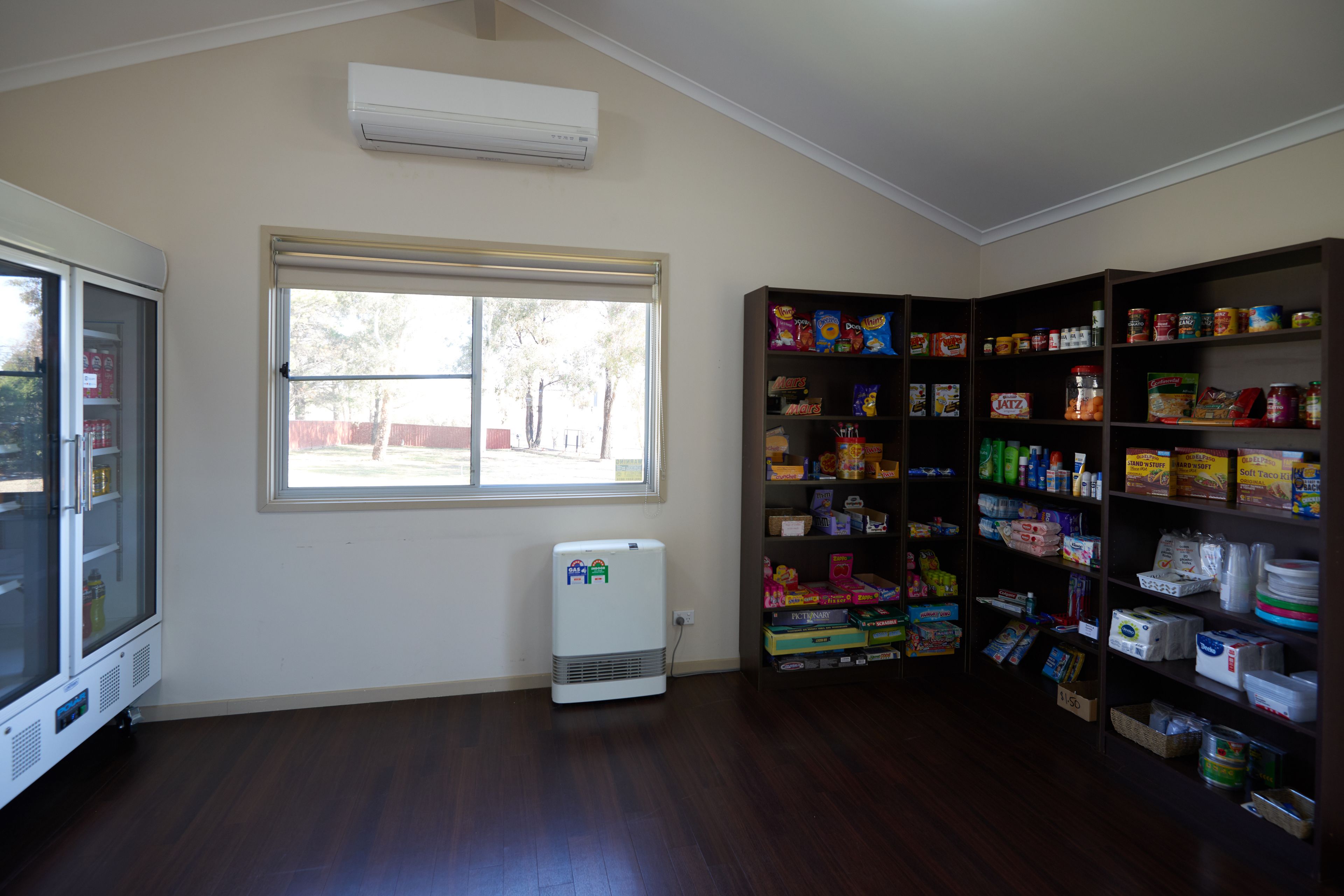 Ein Zimmer mit großem Fenster, einer weißen Klimaanlage und einem Bücherregal voller Gegenstände.