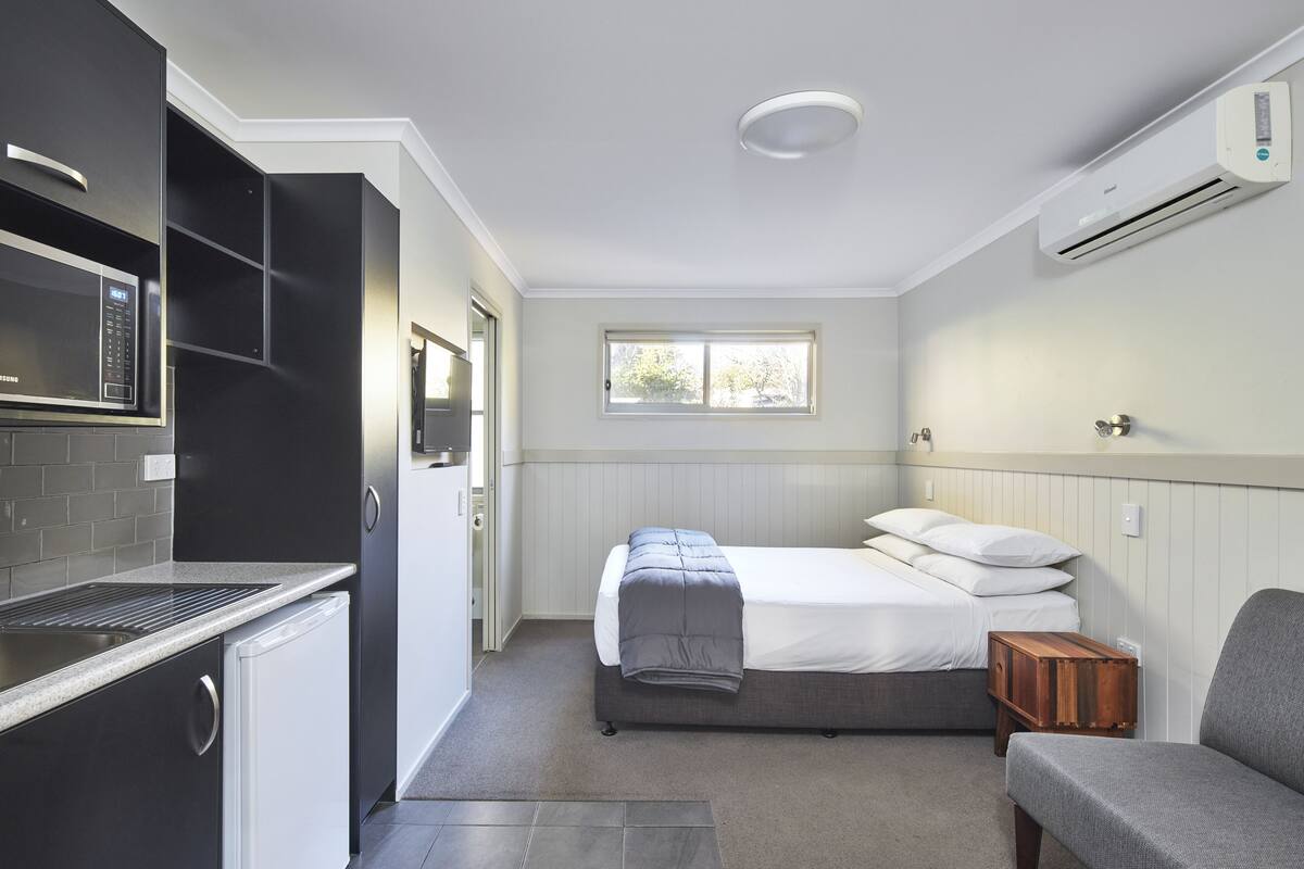 A compact room with a bed, a small sofa, a kitchenette, and a window.