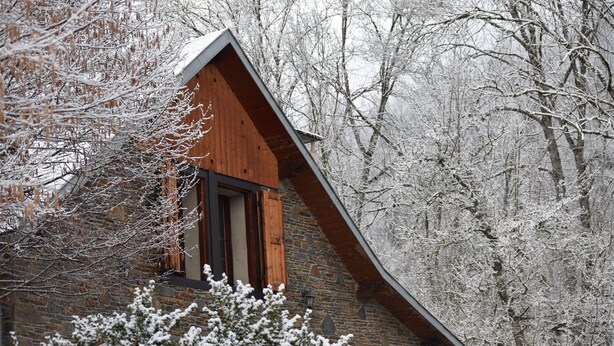 Une cabane en bois, dotée d’un toit à forte pente, entourée d’arbres couverts de neige.