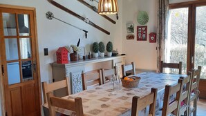 Un espace repas comprenant une table et des chaises en bois, un luminaire suspendu, ainsi qu’un coin cuisine avec une cuisinière et des placards.
