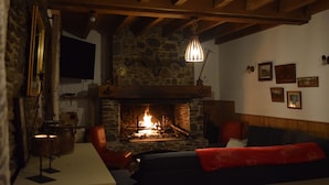 Une pièce chaleureuse avec une cheminée en pierre, des poutres apparentes, un canapé et une table sur laquelle est posée une bougie.