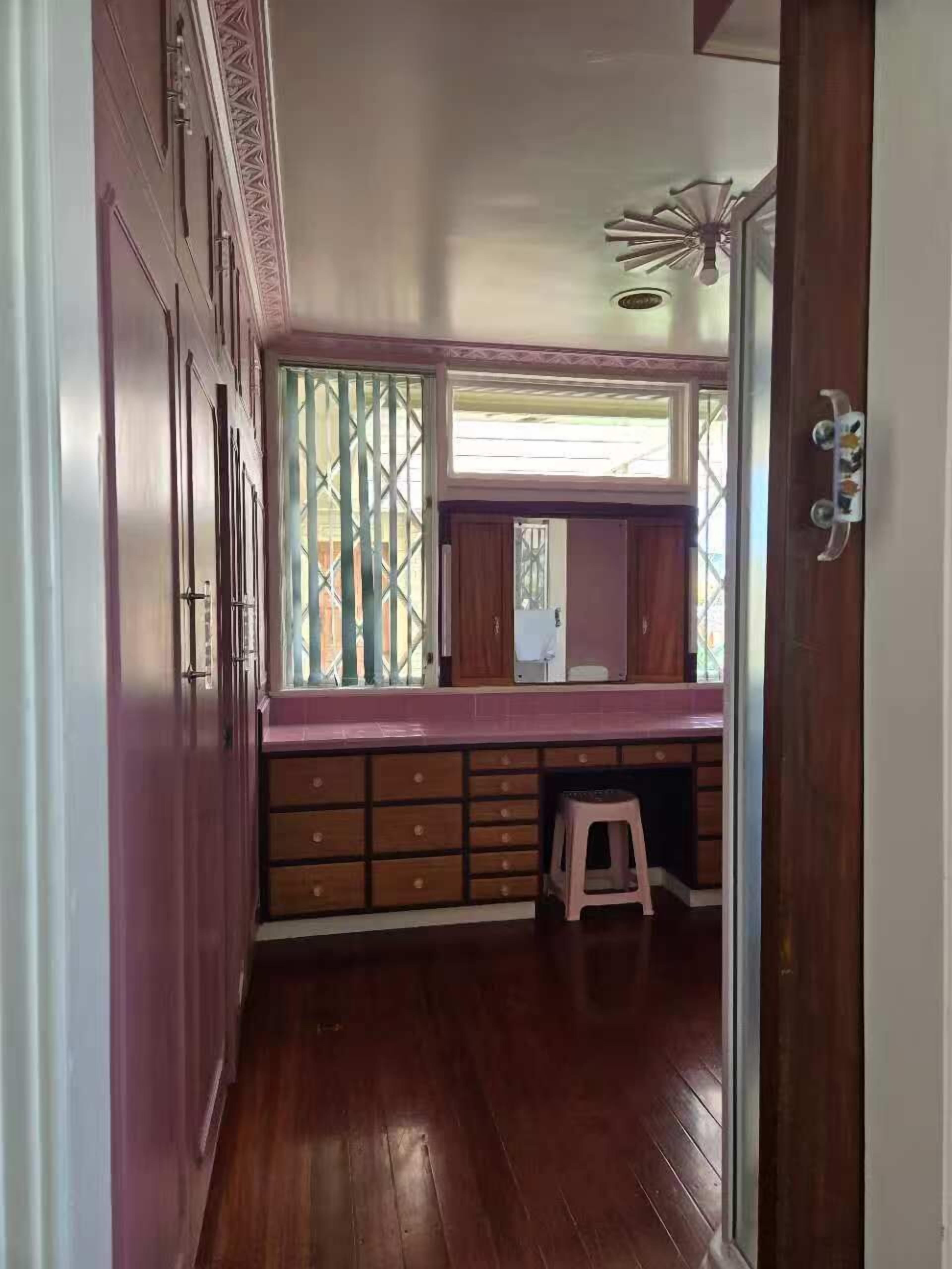A narrow hallway with wooden flooring, a window with green lattice, and a small stool.