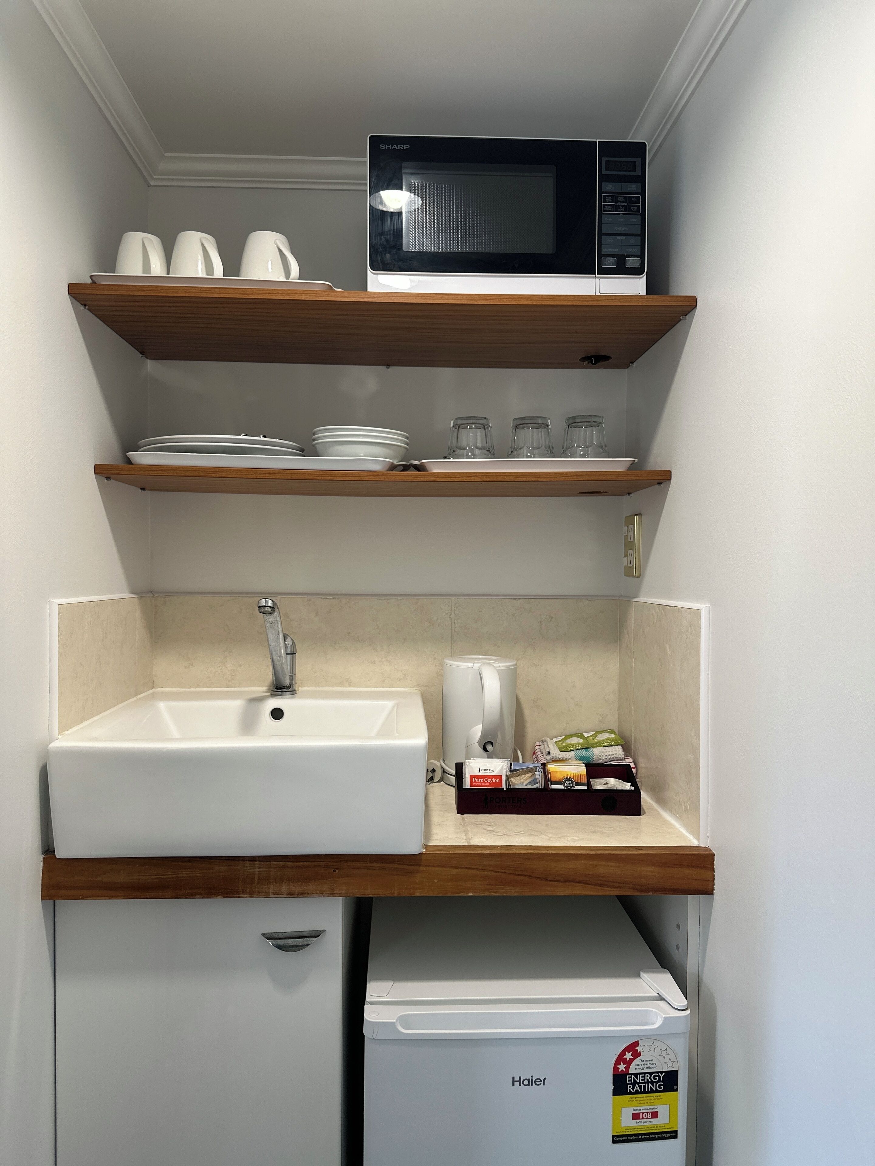 Cocina compacta con microondas, lavabo y estanterías.
