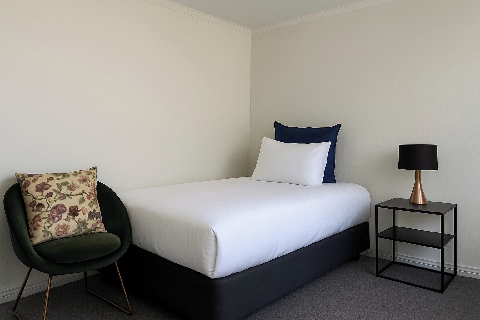 A hotel room with a bed, a chair, and a nightstand with a lamp.