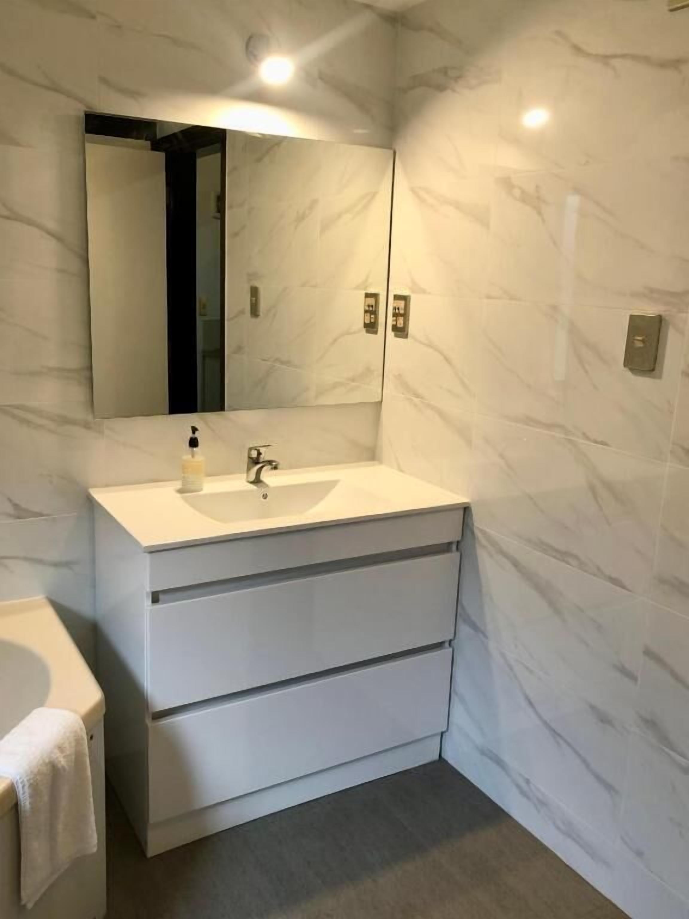 Un bany amb un lavabo blanc, un mirall i parets de marbre.