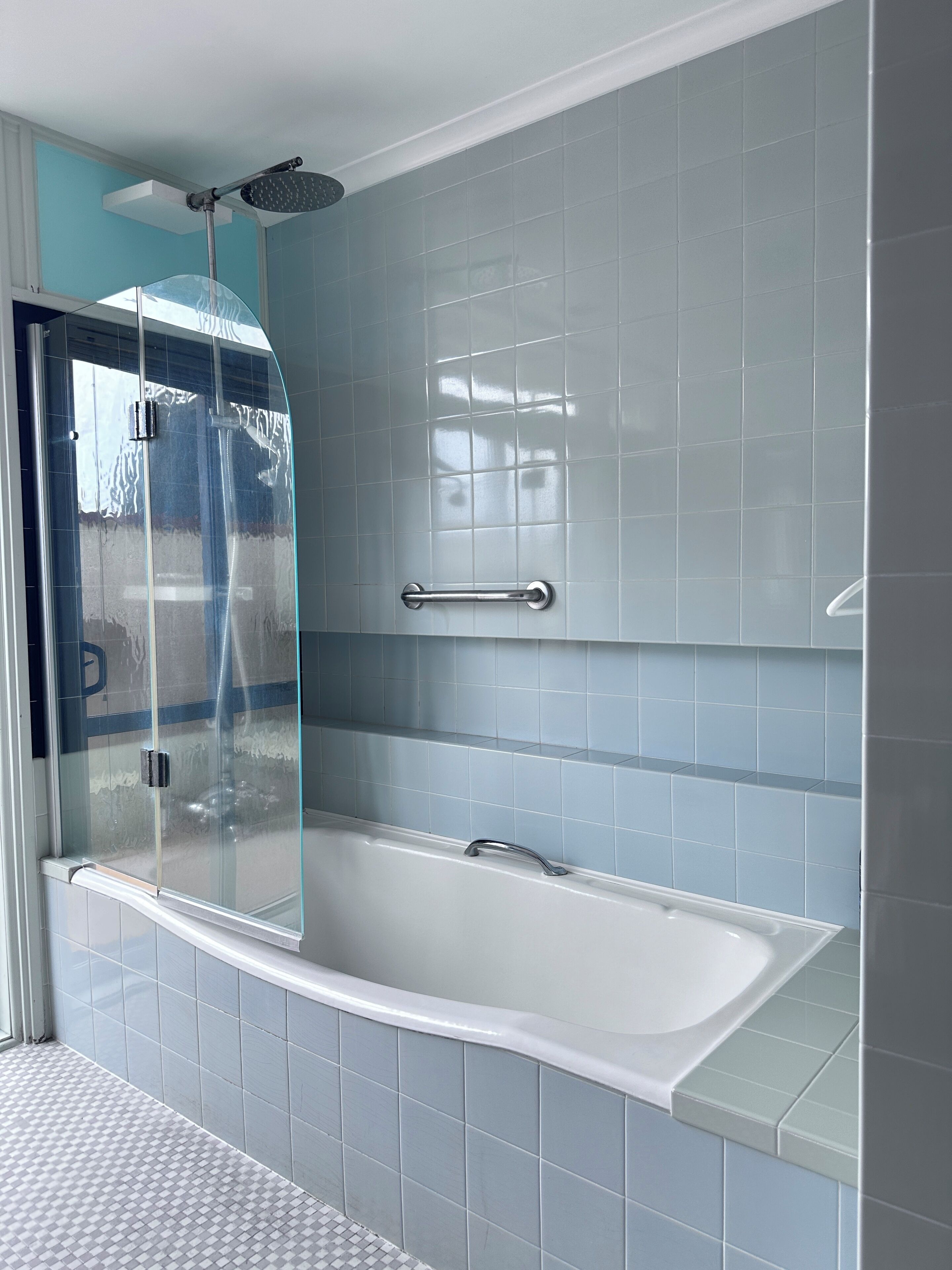 Un baño moderno con ducha envuelta en vidrio, bañera blanca y azulejos azul claro.