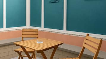 Um alpendre coberto com uma mesa e duas cadeiras, uma parede azul-turquesa decorada com conchas e um chão estampado.