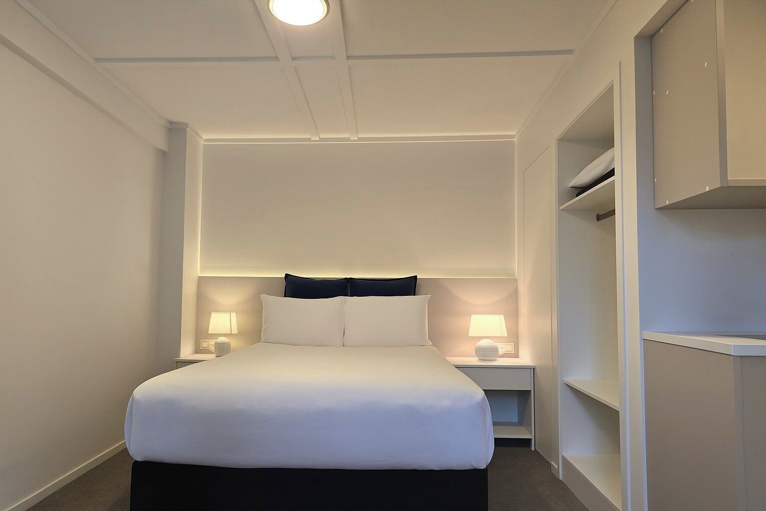 A hotel room with a large bed, two bedside tables with lamps, and built-in shelving.