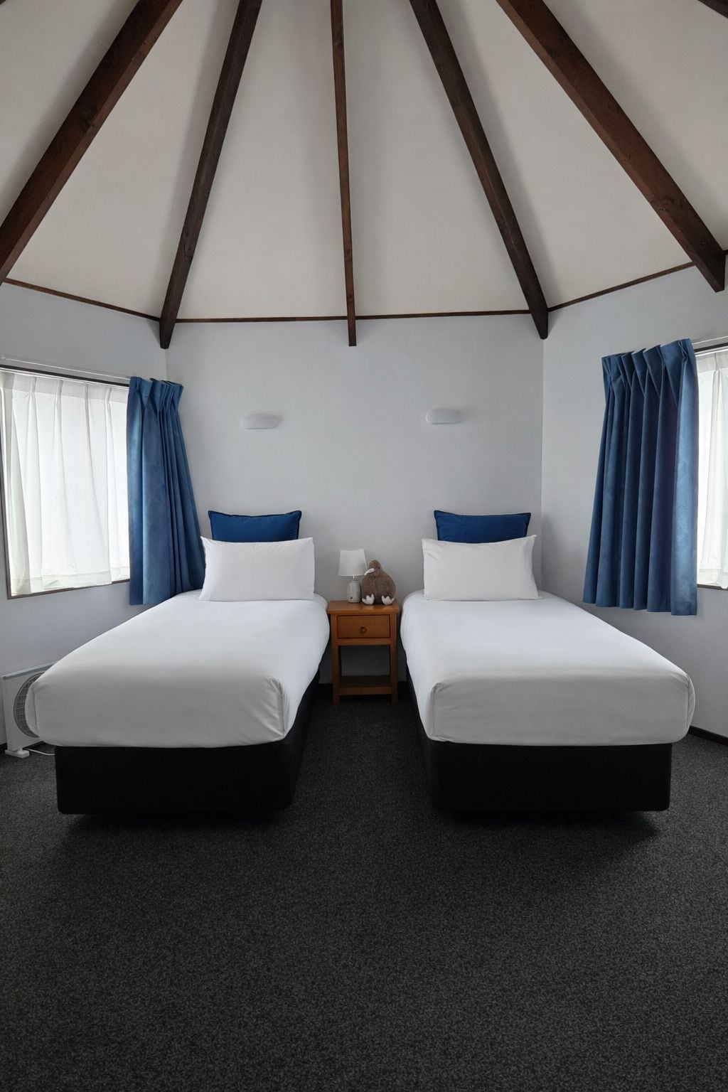 A room with two beds, a nightstand, a lamp, and a window with curtains.