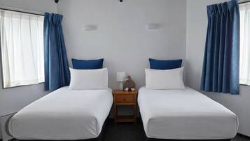 A room with two beds, a nightstand, a lamp, and a window with curtains.