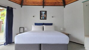 A bedroom with a wooden ceiling, a bed with white bedding and blue pillows, a framed picture on the wall, and a nightstand with a lamp. - Pure Motel (Rotorua)
